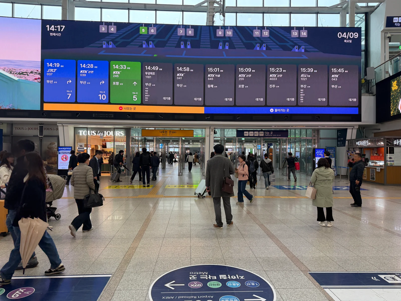 Large departure display in Seoul Station showing train type, number, destination, platform and boarding status above the concourse